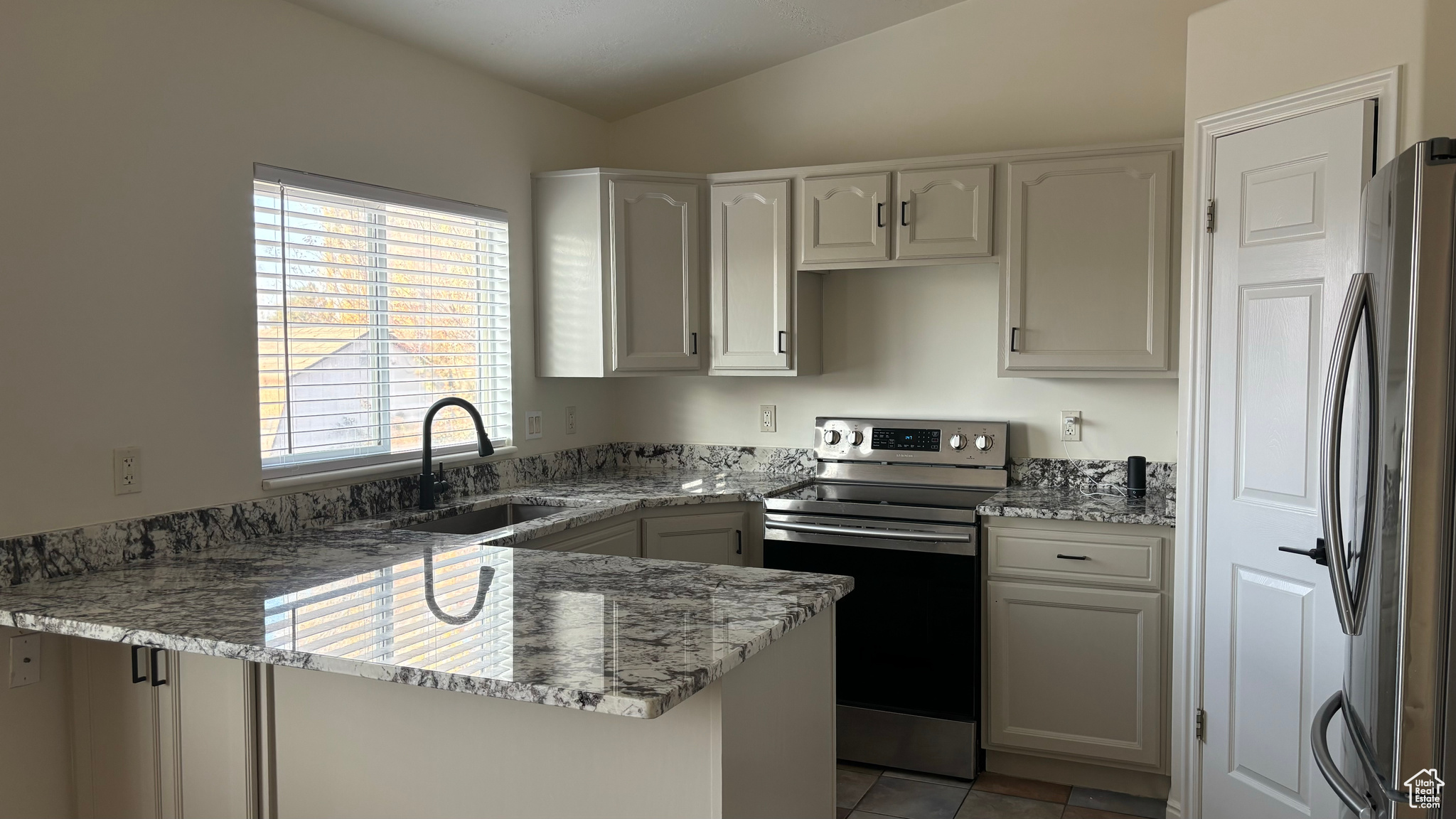 Kitchen with white cabinetry, sink, stainless steel appliances, and lofted ceiling