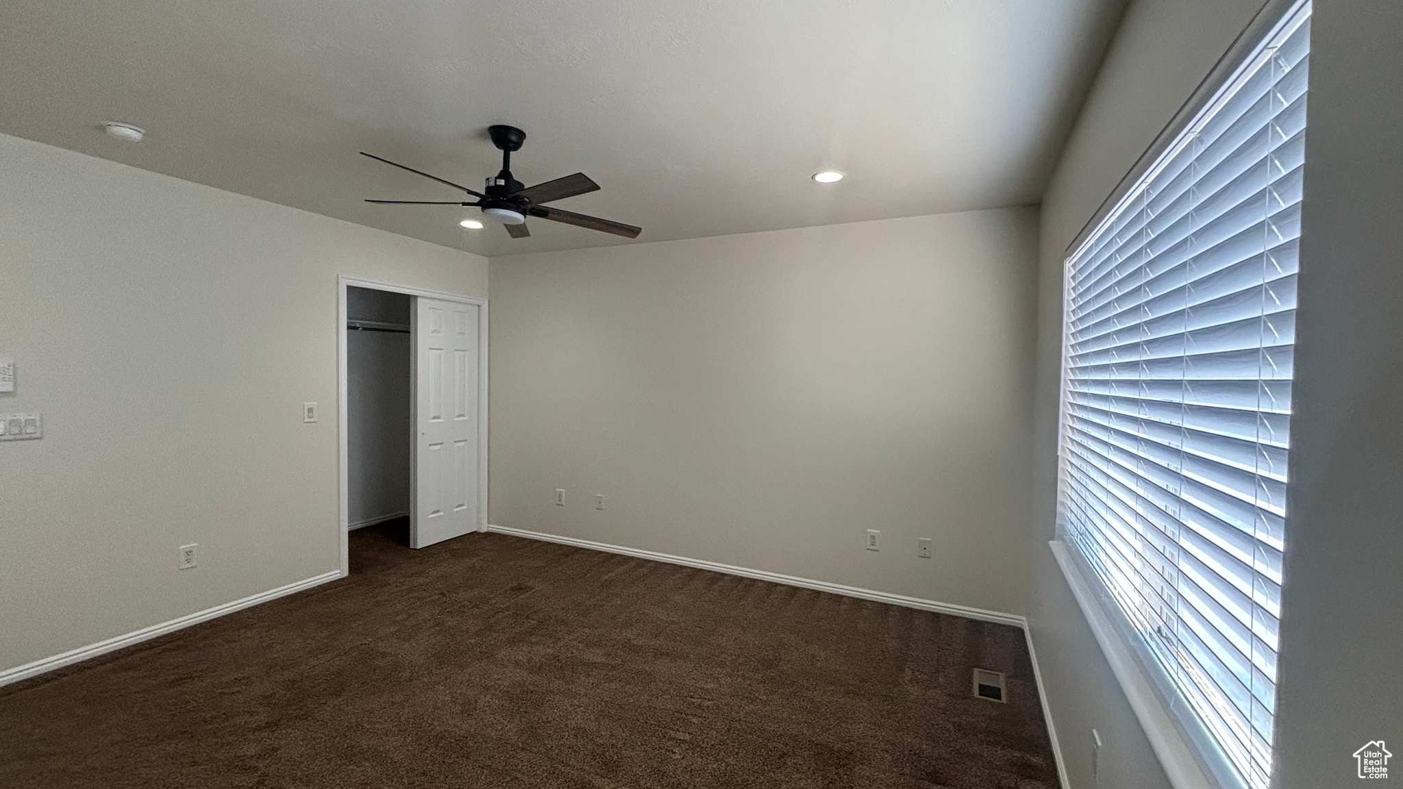 Unfurnished bedroom with ceiling fan, dark carpet, and multiple windows