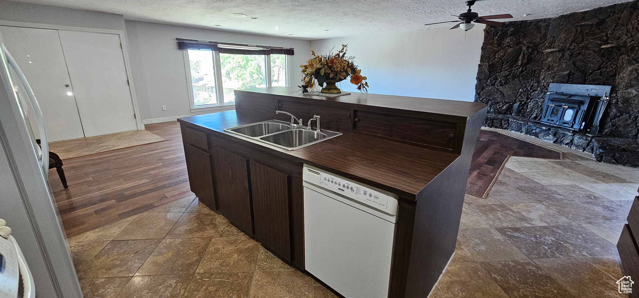 Kitchen featuring ceiling fan, white dishwasher, sink, a wood stove, and a textured ceiling