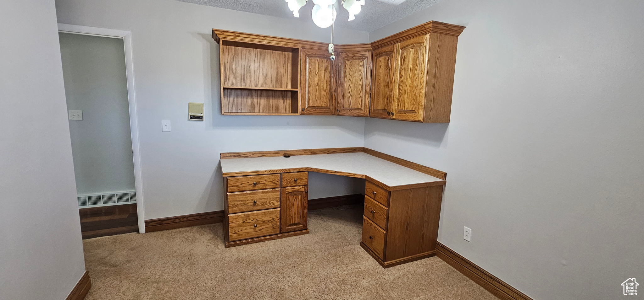 Office space with built in desk, a textured ceiling, and light colored carpet