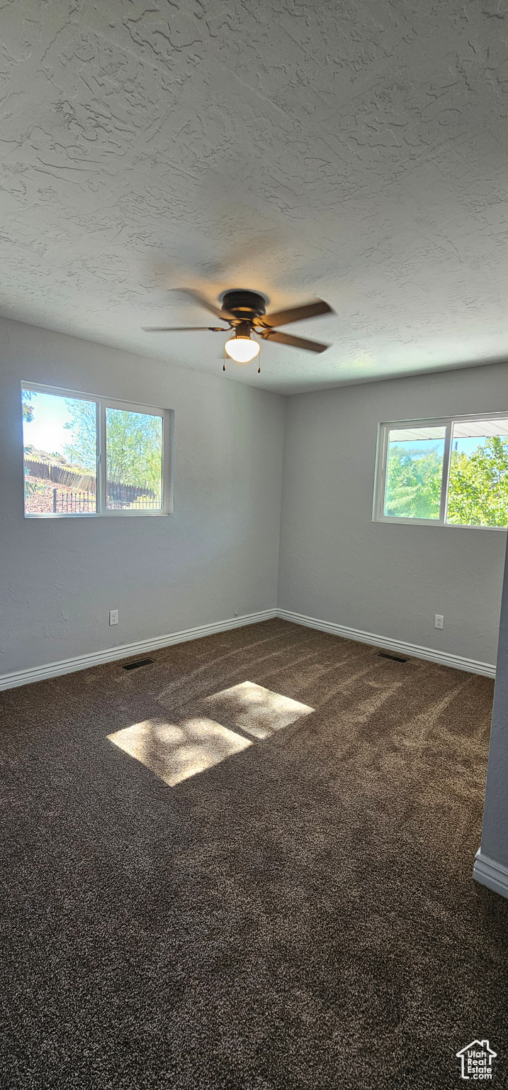 Carpeted empty room featuring ceiling fan and a textured ceiling