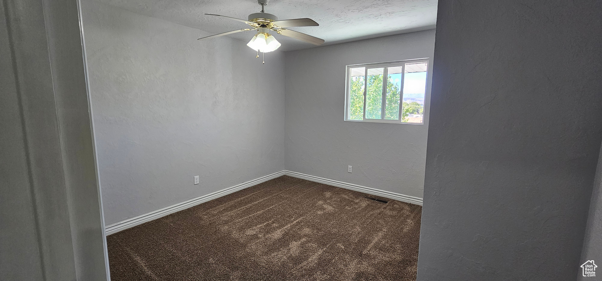 Carpeted empty room featuring ceiling fan and a textured ceiling