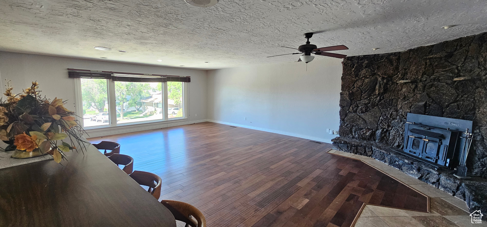 Living room featuring a textured ceiling, hardwood / wood-style flooring, a wood stove, a fireplace, and ceiling fan