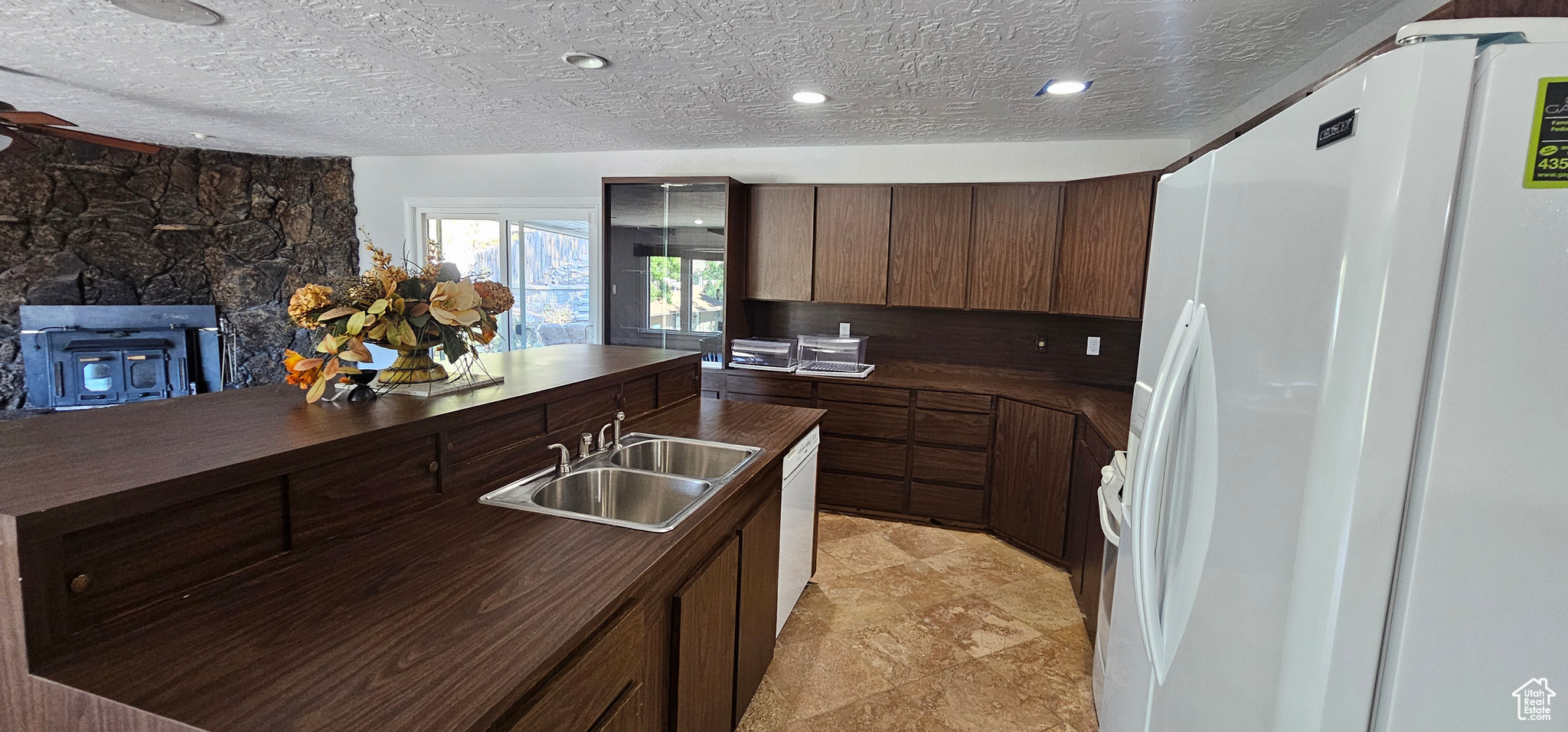 Kitchen with a textured ceiling, sink, a fireplace, white appliances, and dark brown cabinetry