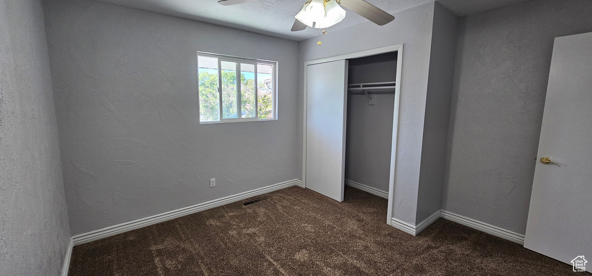 Unfurnished bedroom featuring a closet, dark colored carpet, and ceiling fan