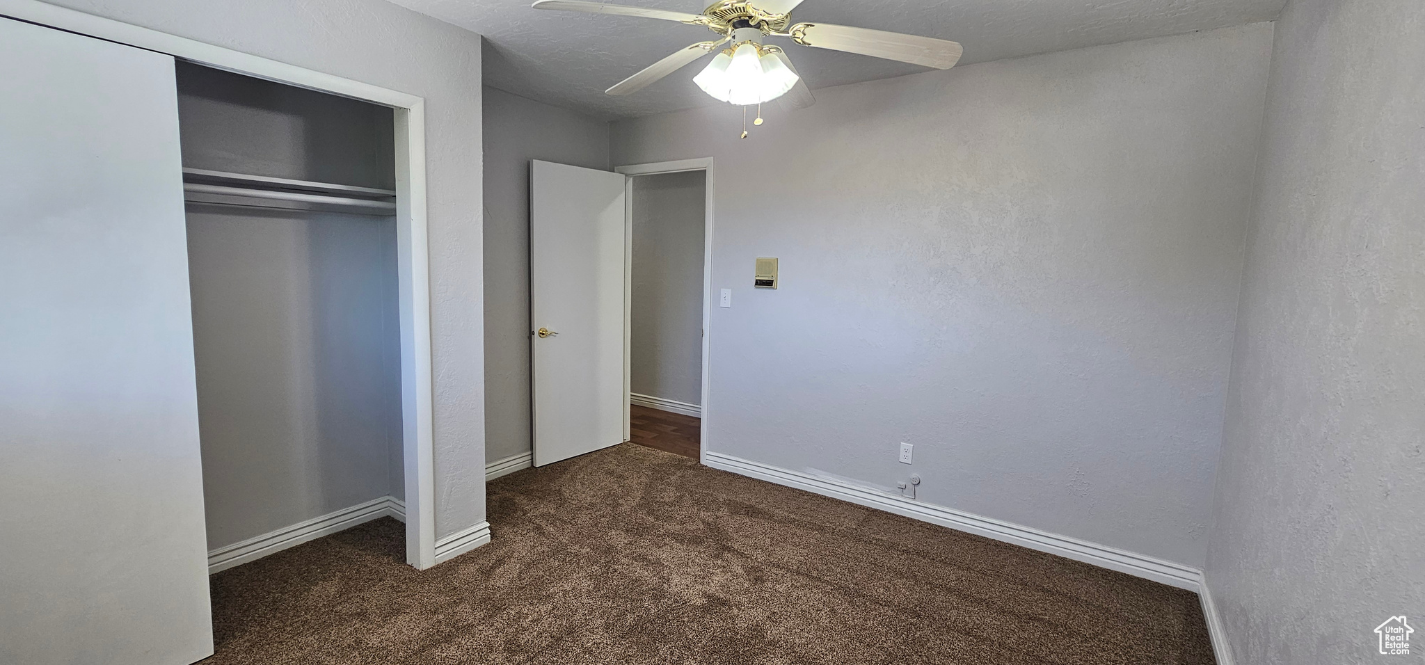 Unfurnished bedroom with ceiling fan, a textured ceiling, a closet, and dark carpet