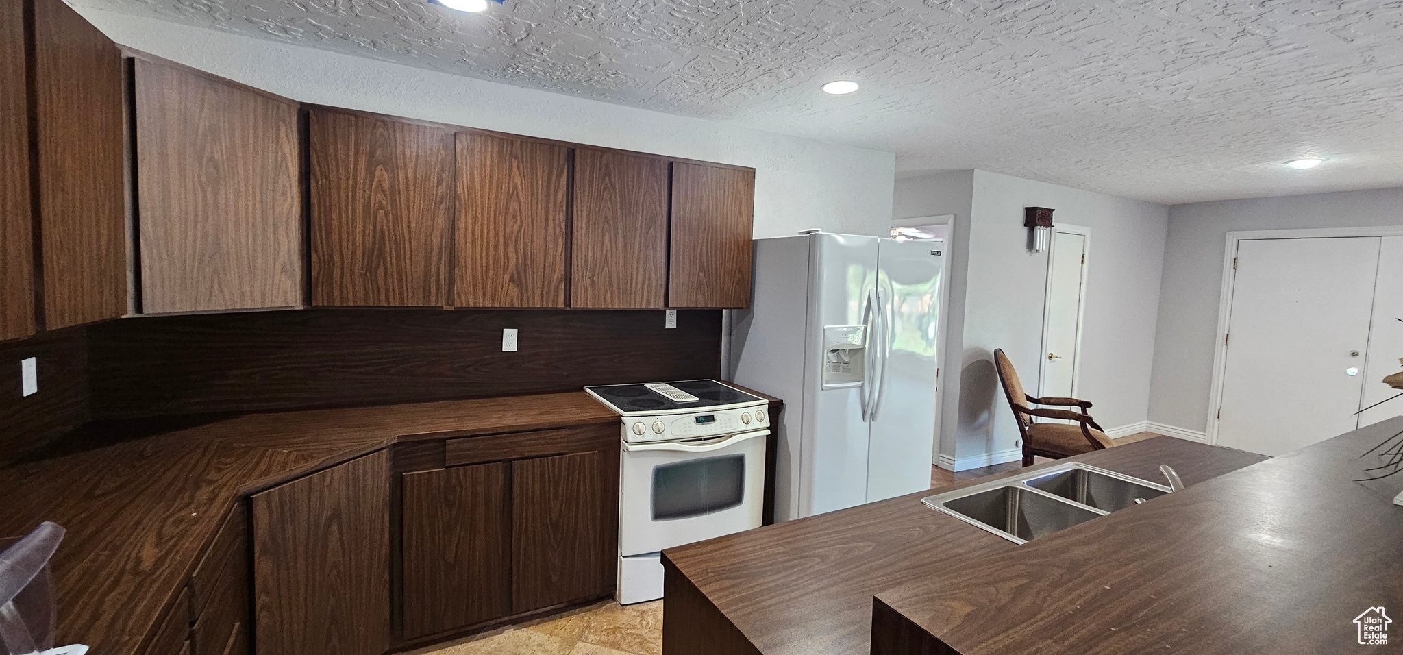 Kitchen featuring white appliances, a textured ceiling, dark brown cabinetry, and sink