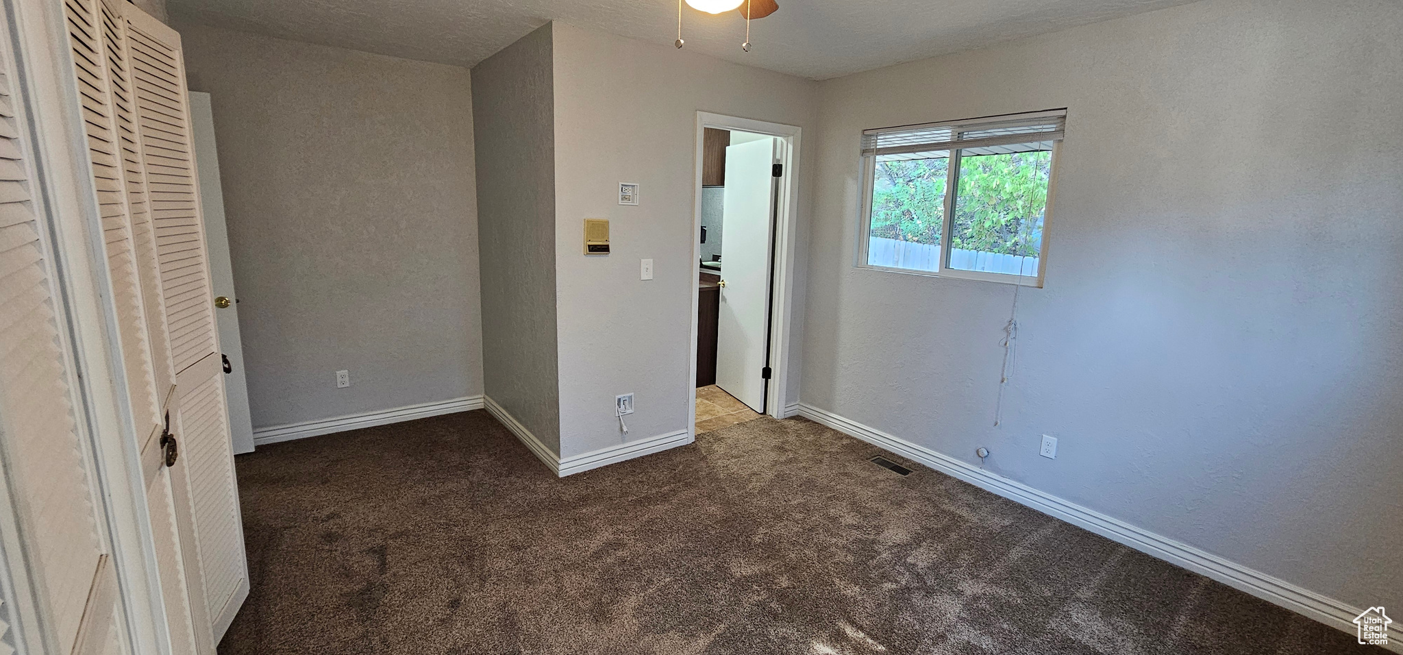 Unfurnished bedroom with dark carpet and ceiling fan