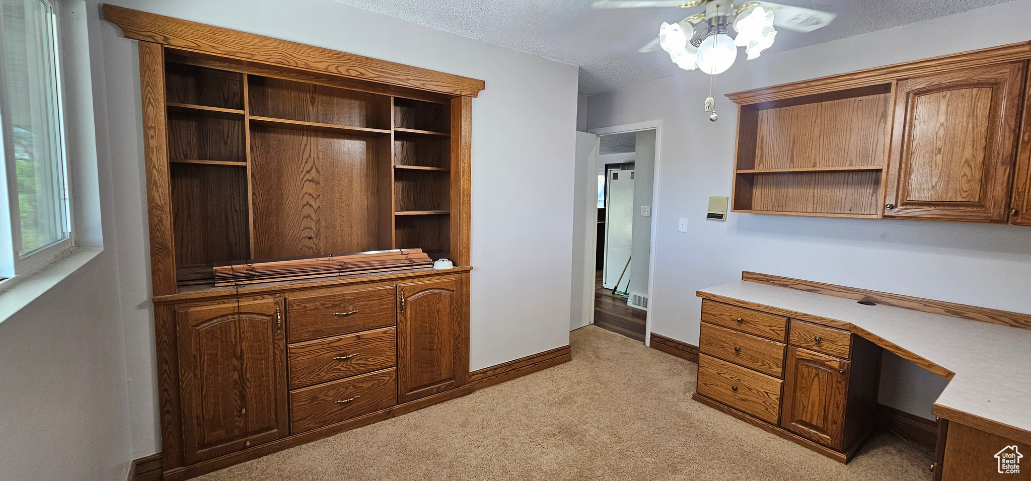 Office area with built in desk, ceiling fan, light colored carpet, and a textured ceiling