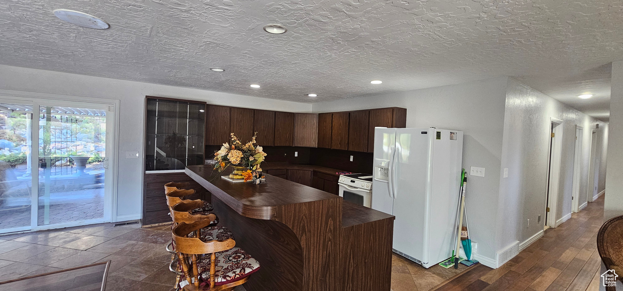 Kitchen featuring dark brown cabinetry, white appliances, a kitchen island, a textured ceiling, and dark wood-type flooring