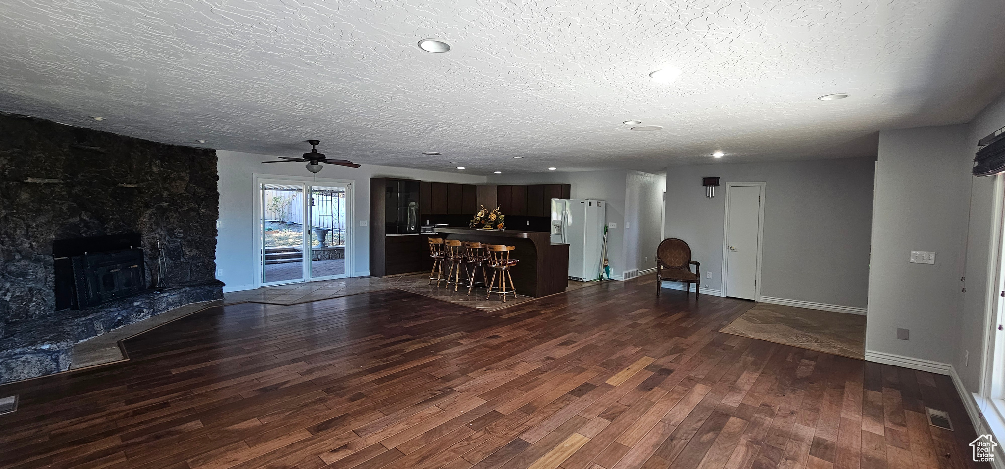 Unfurnished living room with ceiling fan, a textured ceiling, a fireplace, and dark hardwood / wood-style flooring