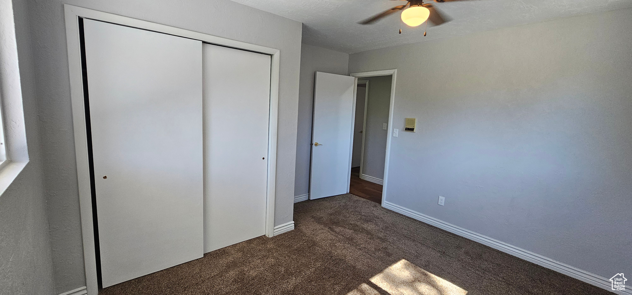 Unfurnished bedroom with ceiling fan, a closet, and dark colored carpet