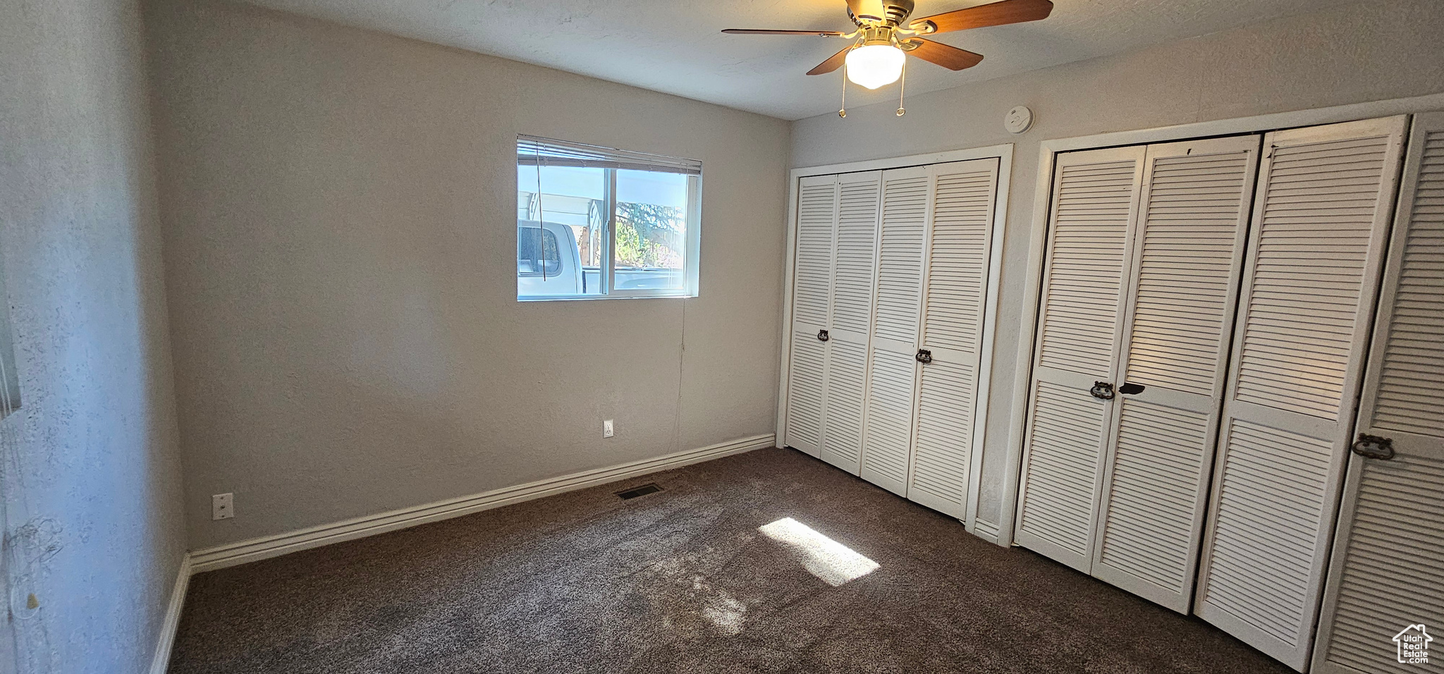 Unfurnished bedroom with ceiling fan, multiple closets, and dark carpet