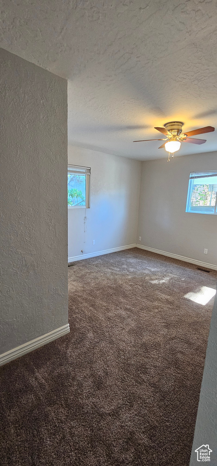 Spare room with ceiling fan, a textured ceiling, and carpet