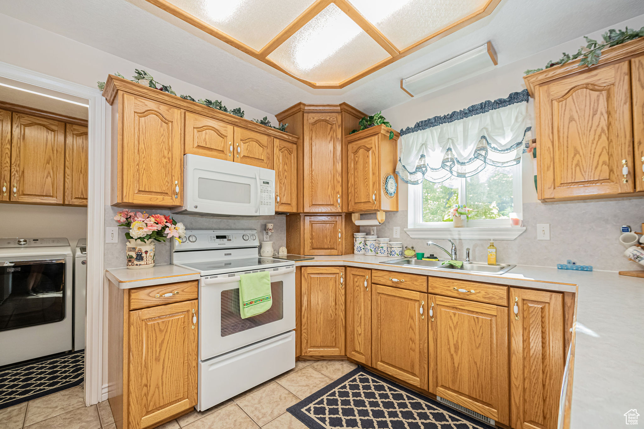 Kitchen featuring backsplash, independent washer and dryer, sink, light tile patterned flooring, and white appliances