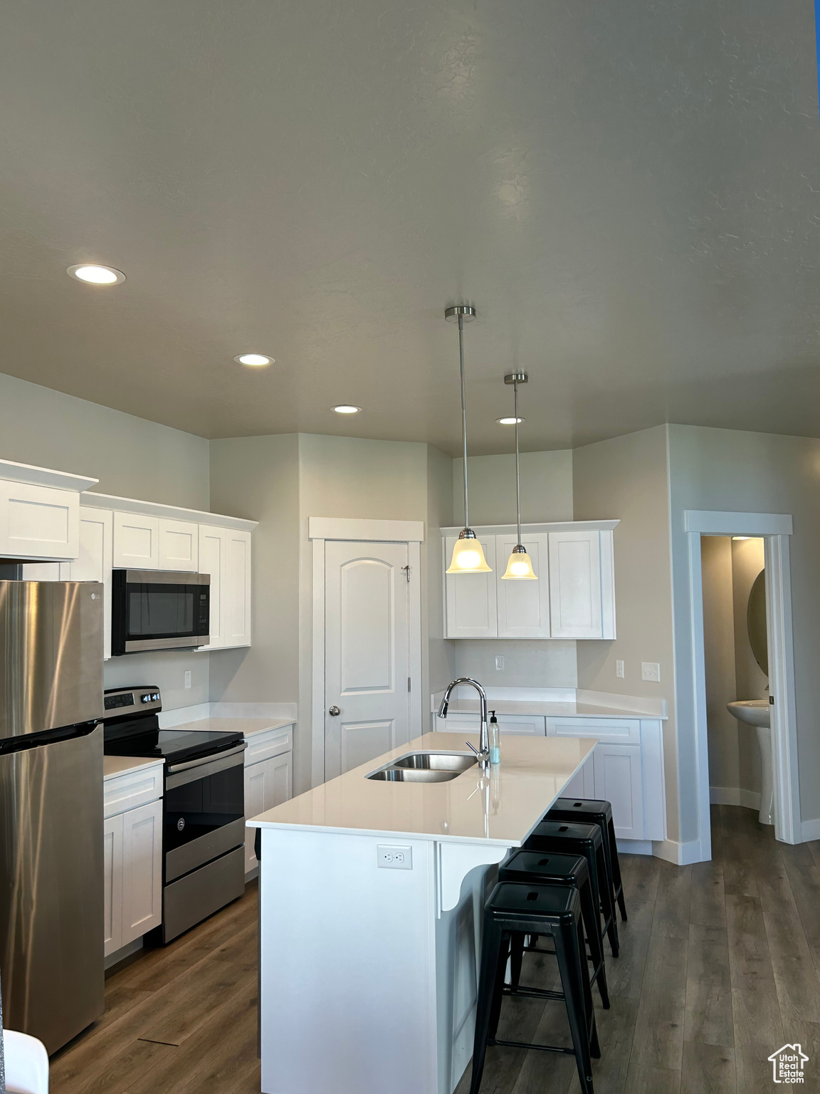 Kitchen with dark wood-type flooring, hanging light fixtures, an island with sink, white cabinets, and appliances with stainless steel finishes