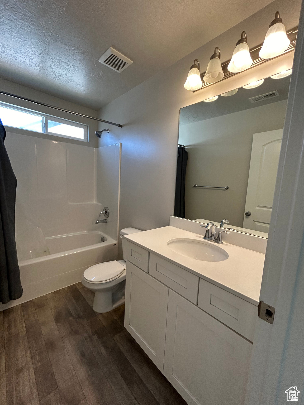 Full bathroom featuring wood-type flooring, toilet, a textured ceiling, vanity, and shower / tub combo