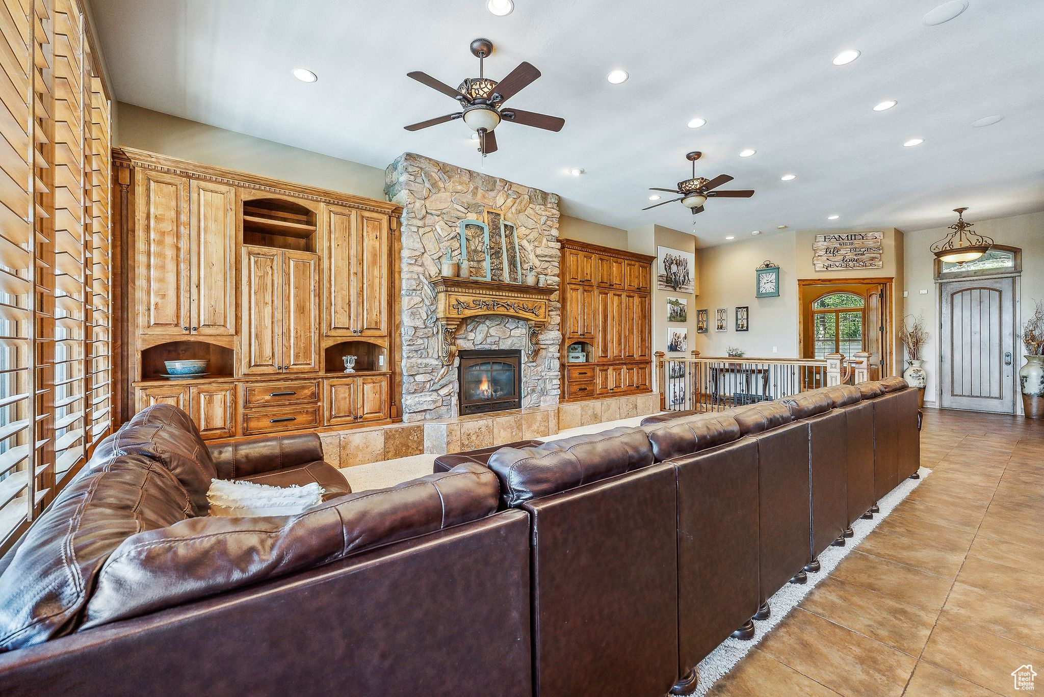 Living room with light tile patterned floors, ceiling fan, and a stone fireplace