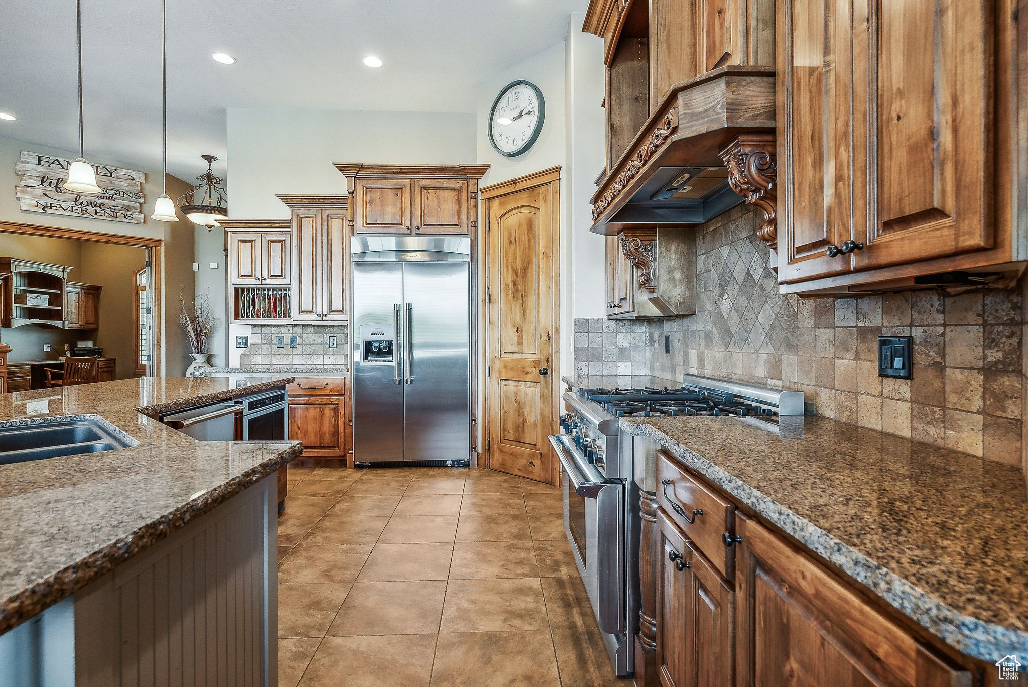 Kitchen with decorative light fixtures, light tile patterned floors, high quality appliances, decorative backsplash, and dark stone countertops