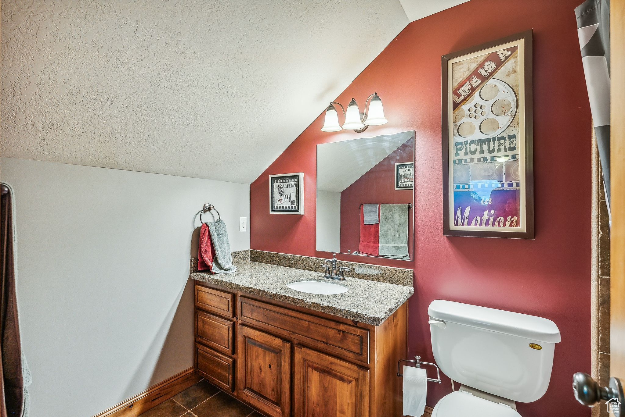 Bathroom featuring tile patterned flooring, a textured ceiling, vaulted ceiling, toilet, and vanity