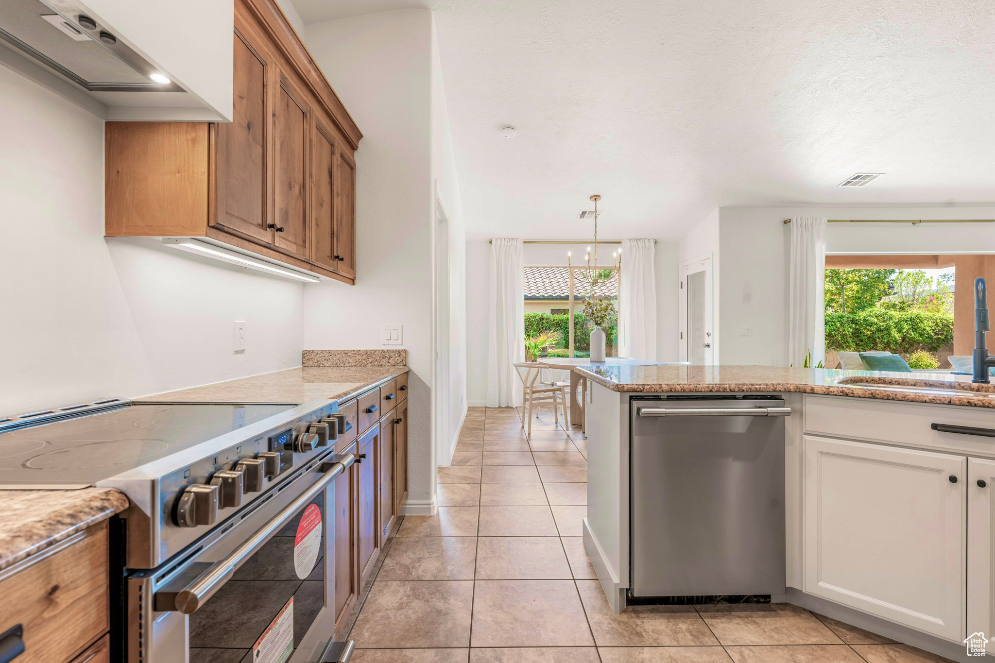 Kitchen featuring appliances with stainless steel finishes, plenty of natural light, light stone counters, and an inviting chandelier