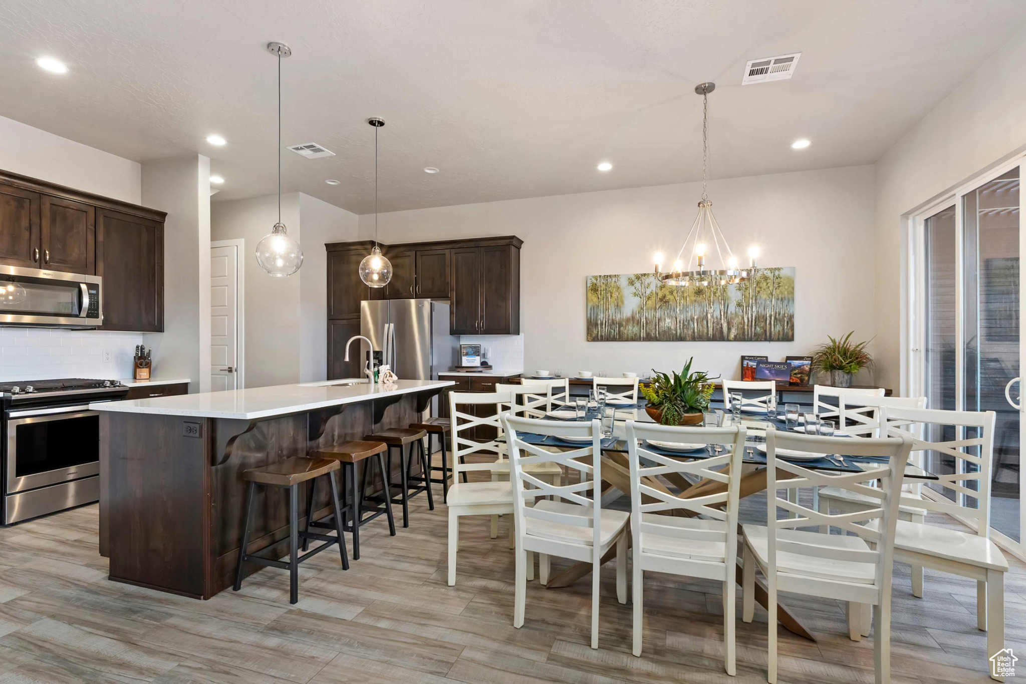 Kitchen featuring light hardwood / wood-style floors, appliances with stainless steel finishes, a center island with sink, and decorative light fixtures