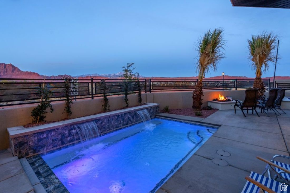 Pool at dusk featuring pool water feature, a patio, and a fire pit