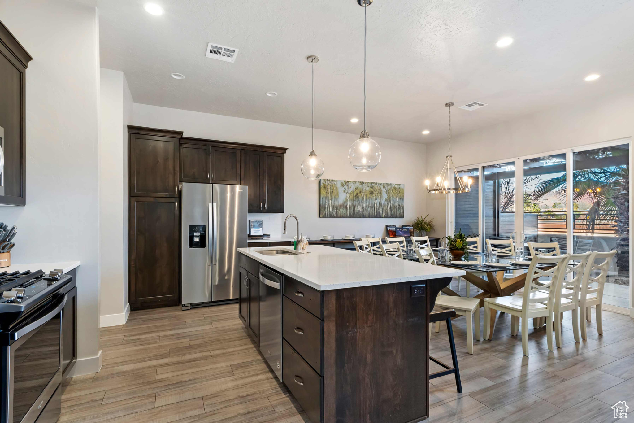 Kitchen with sink, dark brown cabinets, a kitchen island with sink, stainless steel appliances, and pendant lighting