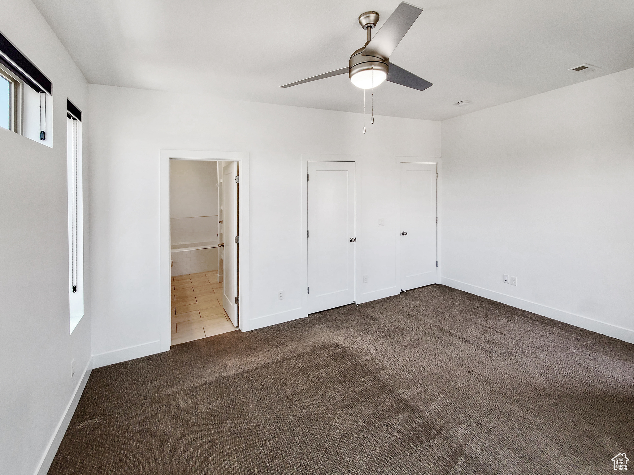 Unfurnished bedroom with light colored carpet, ensuite bath, and ceiling fan