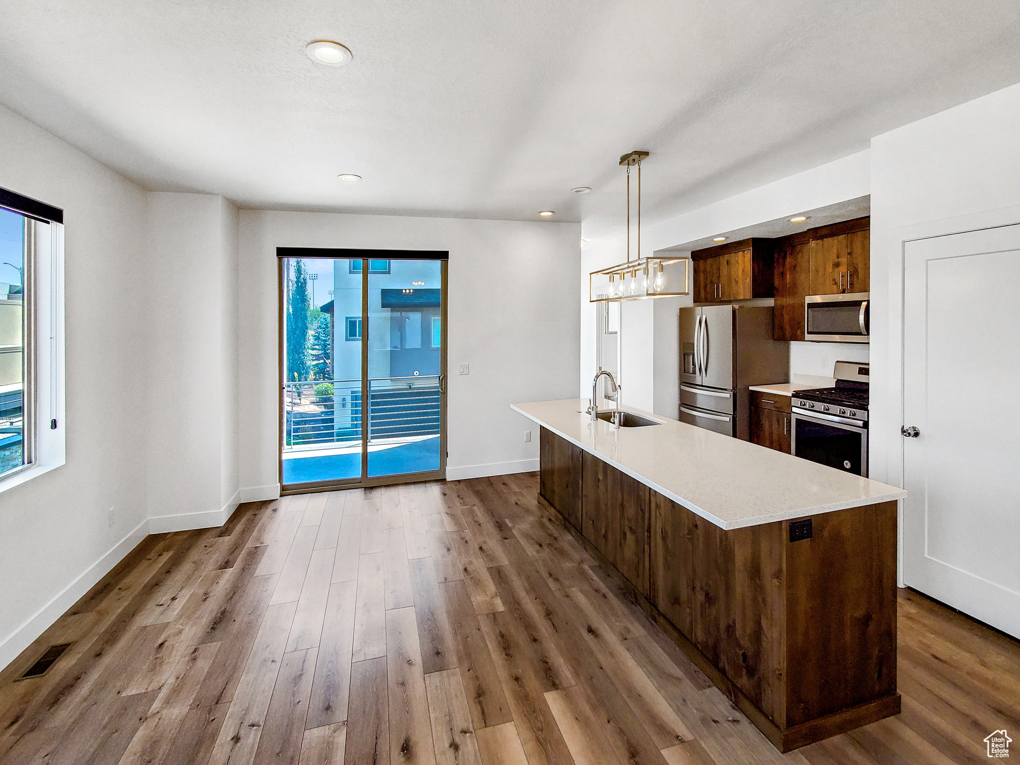 Kitchen with hardwood / wood-style floors, appliances with stainless steel finishes, sink, pendant lighting, and a kitchen island with sink