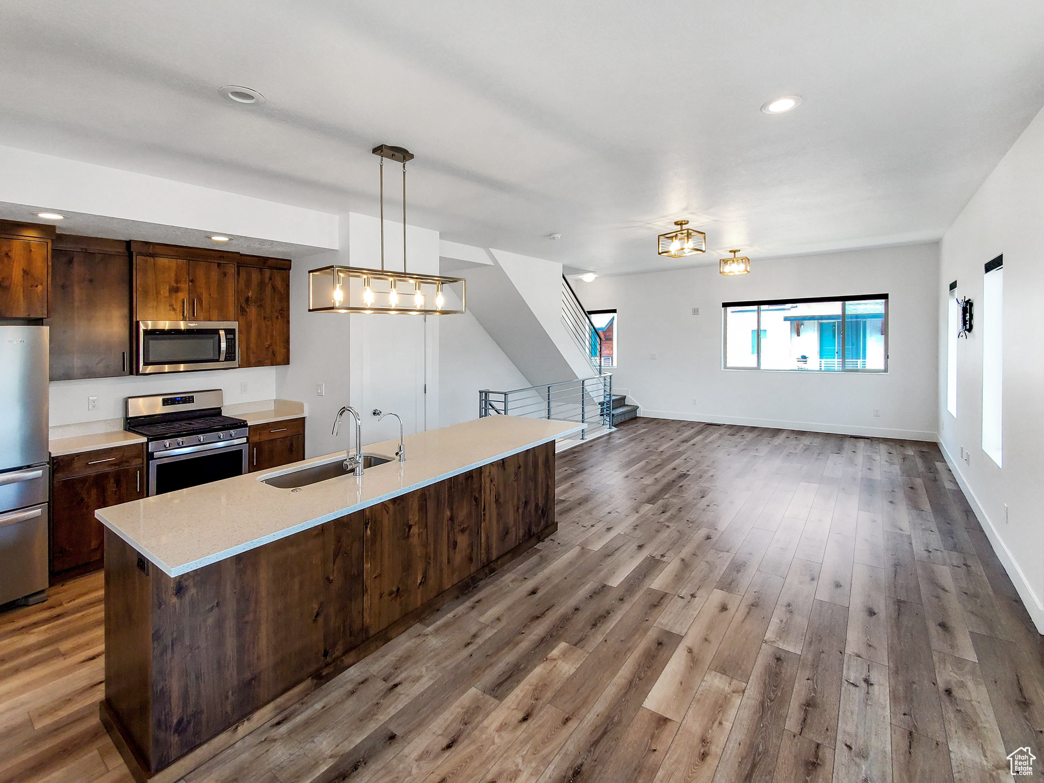 Kitchen with hardwood / wood-style floors, decorative light fixtures, sink, light stone countertops, and appliances with stainless steel finishes