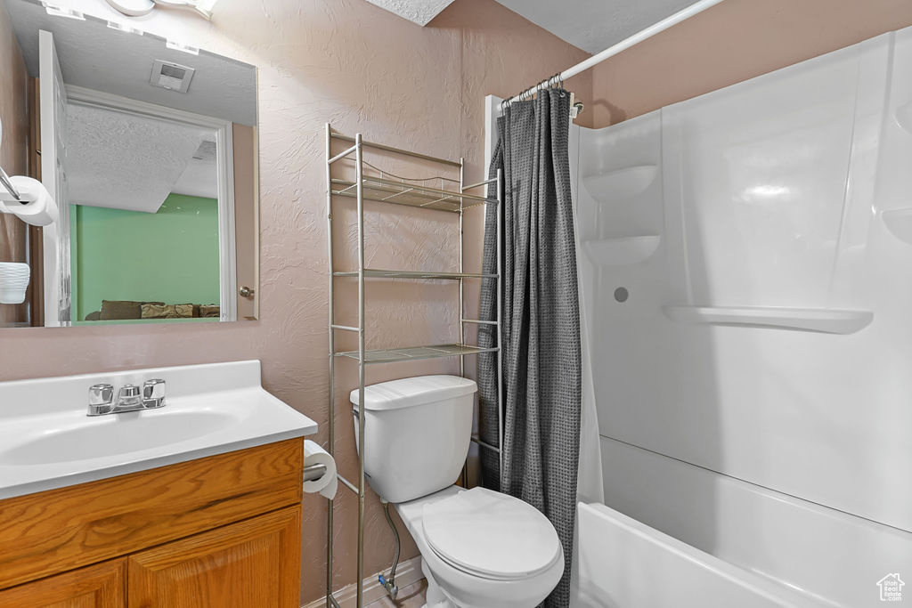 Full bathroom featuring vanity, toilet, shower / bath combo with shower curtain, and a textured ceiling