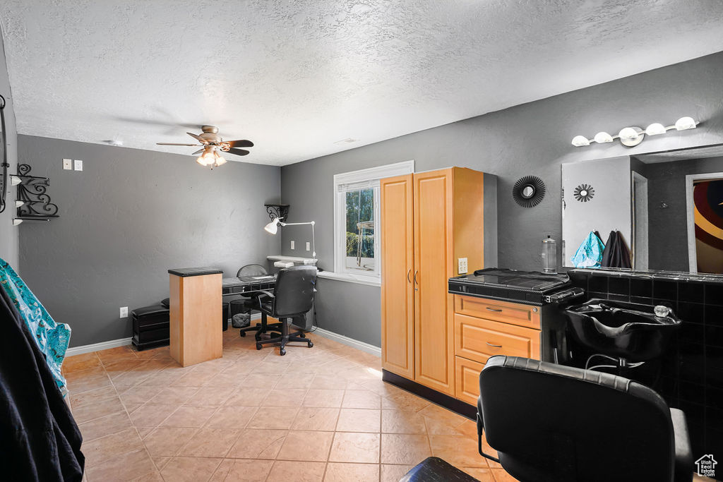 Office with a textured ceiling, light tile patterned floors, and ceiling fan