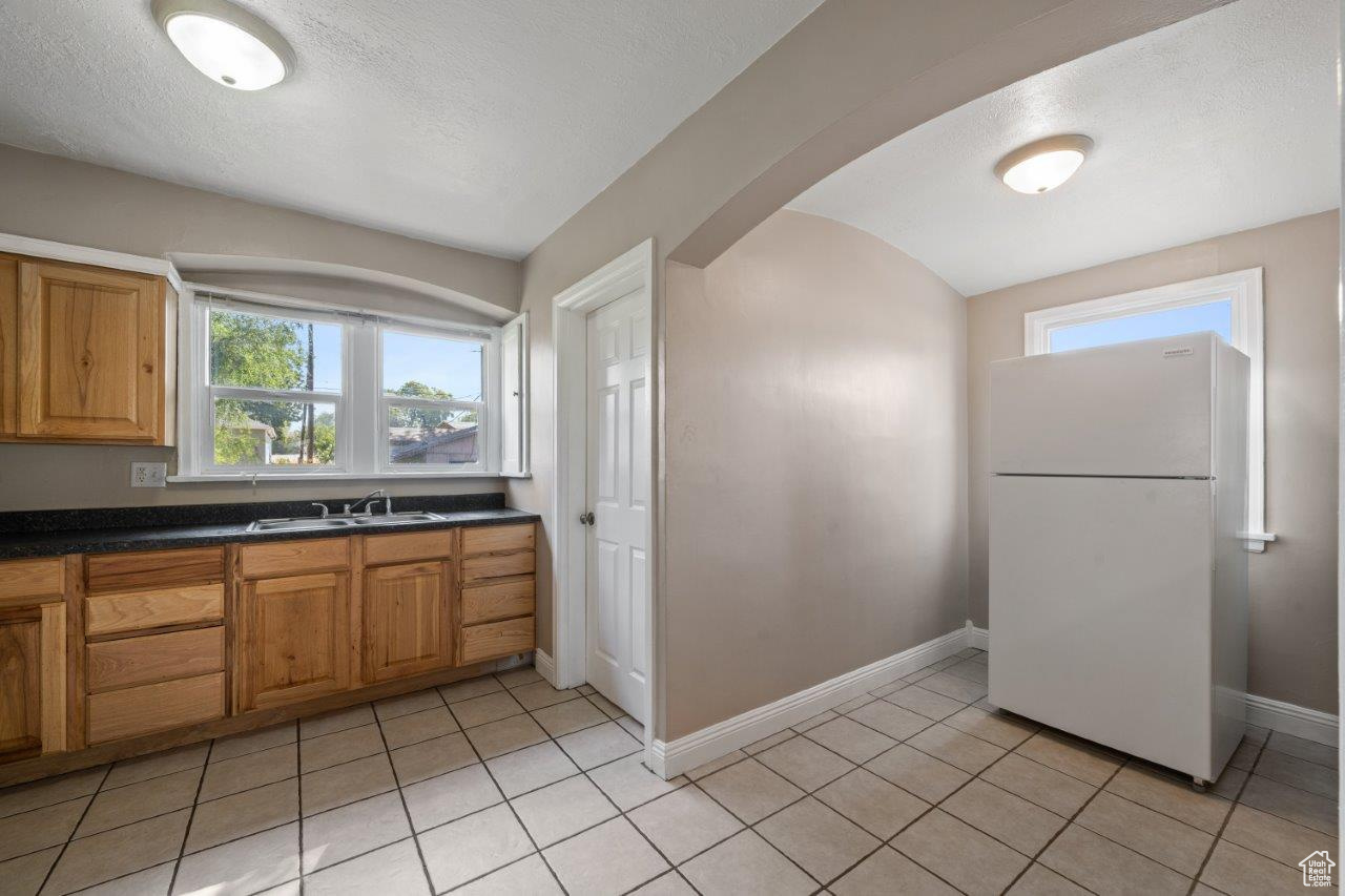 Kitchen with white refrigerator, a textured ceiling, sink, and light tile patterned flooring