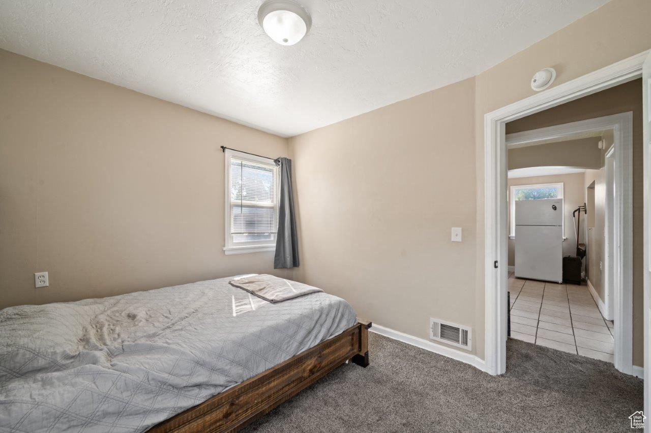 Bedroom featuring carpet, a textured ceiling, and white fridge