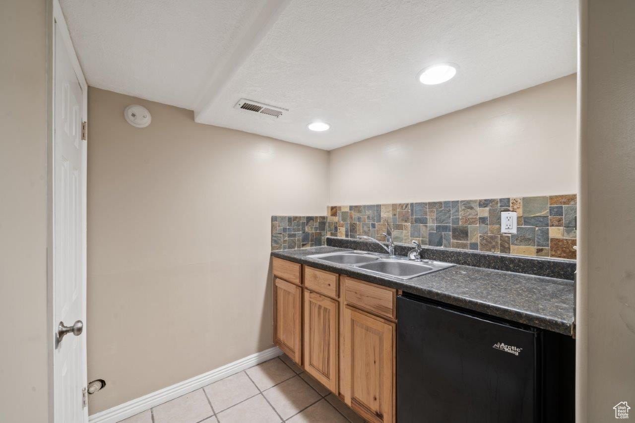 Kitchen featuring a textured ceiling, dishwasher, light tile patterned floors, tasteful backsplash, and sink