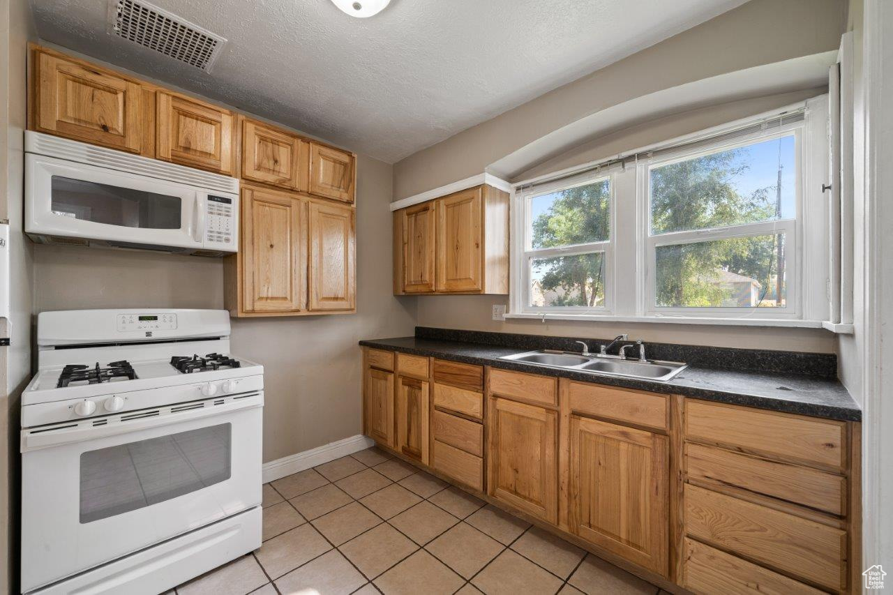 Kitchen featuring white appliances, light tile patterned floors, a textured ceiling, and sink