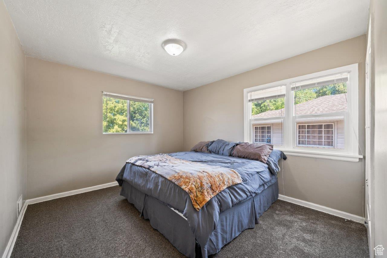 Bedroom featuring a textured ceiling, dark colored carpet, and multiple windows