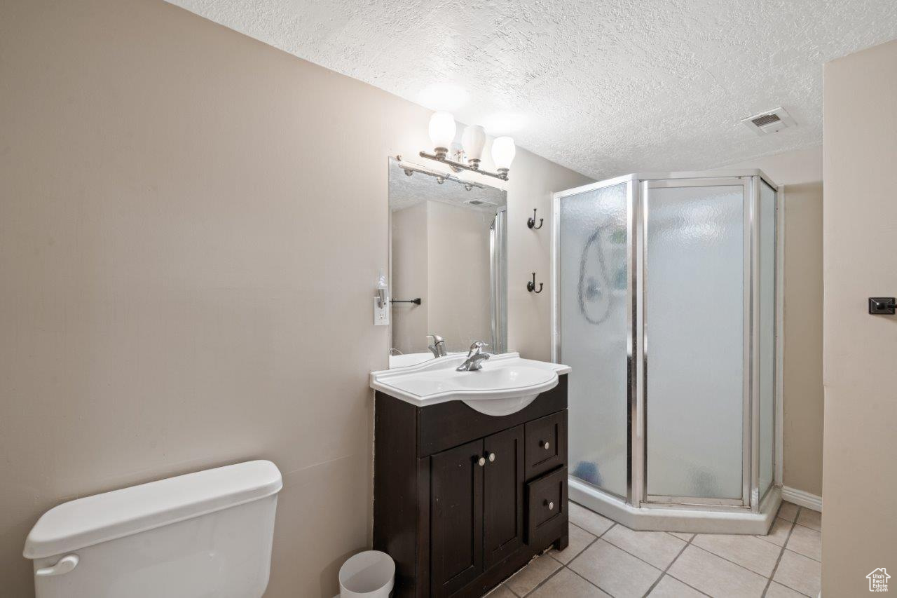 Bathroom featuring a textured ceiling, vanity, an enclosed shower, toilet, and tile patterned floors