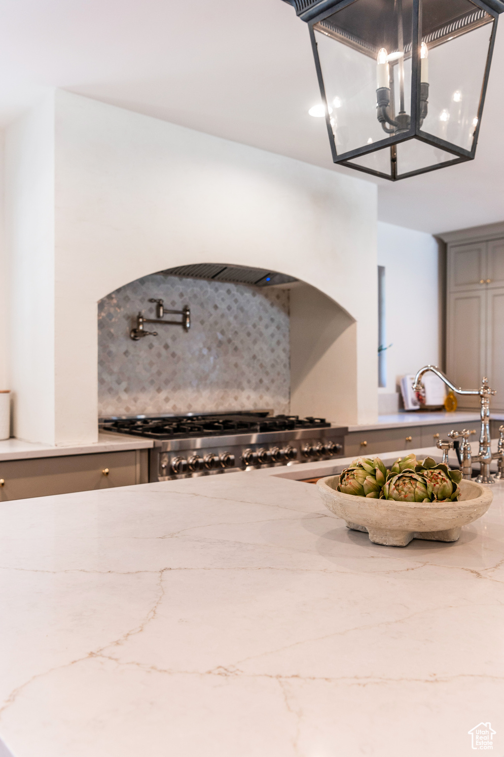 Interior space with tasteful backsplash, gray cabinetry, stainless steel range, an inviting chandelier, and light stone countertops