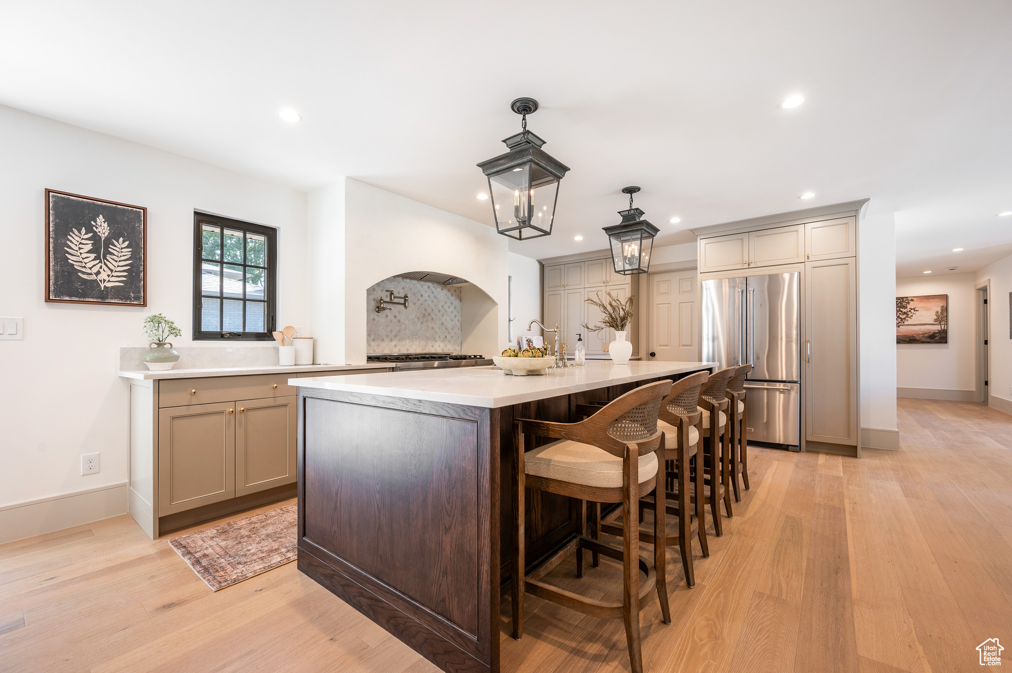 Kitchen with an island with sink, light hardwood / wood-style floors, built in fridge, and hanging light fixtures