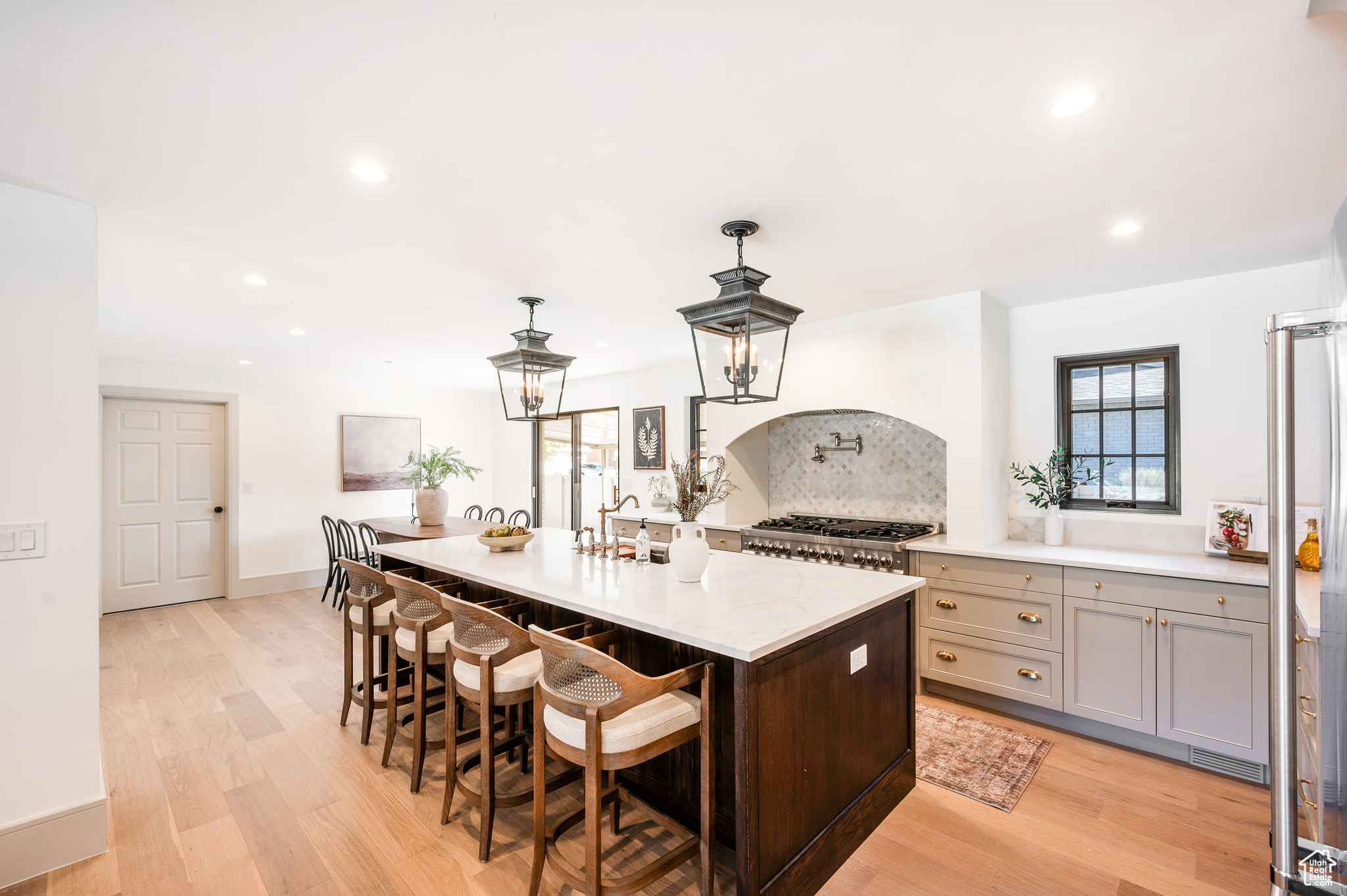 Kitchen with decorative backsplash, light hardwood / wood-style floors, gray cabinetry, stainless steel stove, and decorative light fixtures