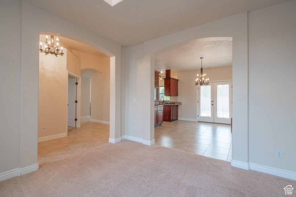 Unfurnished living room with an inviting chandelier, light carpet, french doors, and sink