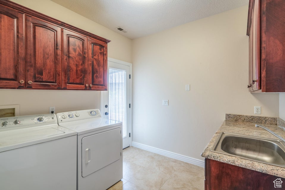 Laundry area featuring a textured ceiling, cabinets, separate washer and dryer, sink, and light tile patterned flooring