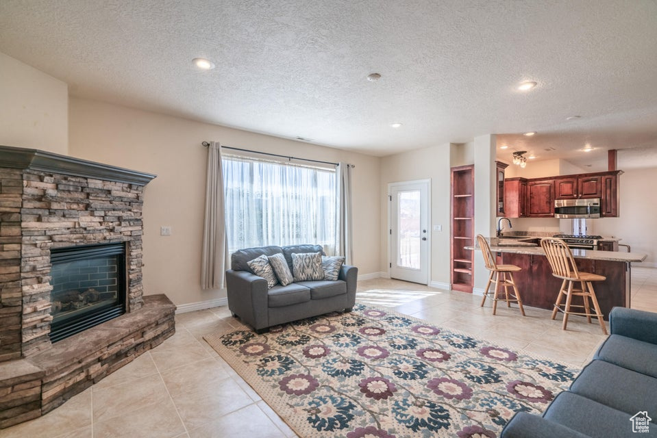 Living room with a textured ceiling, sink, a stone fireplace, and light tile patterned floors