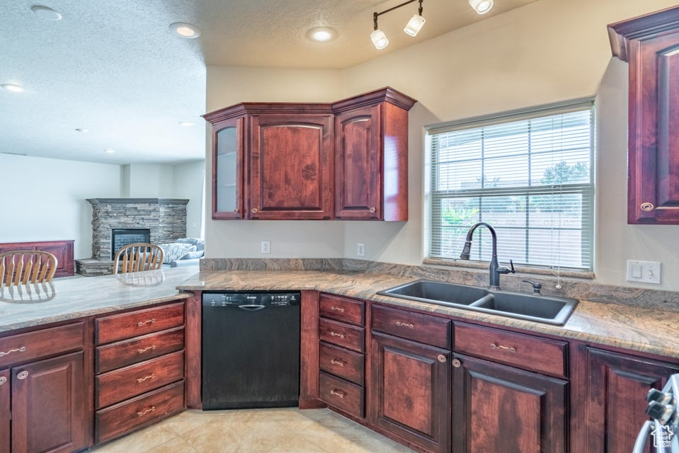 Kitchen with a textured ceiling, dishwasher, a stone fireplace, sink, and rail lighting