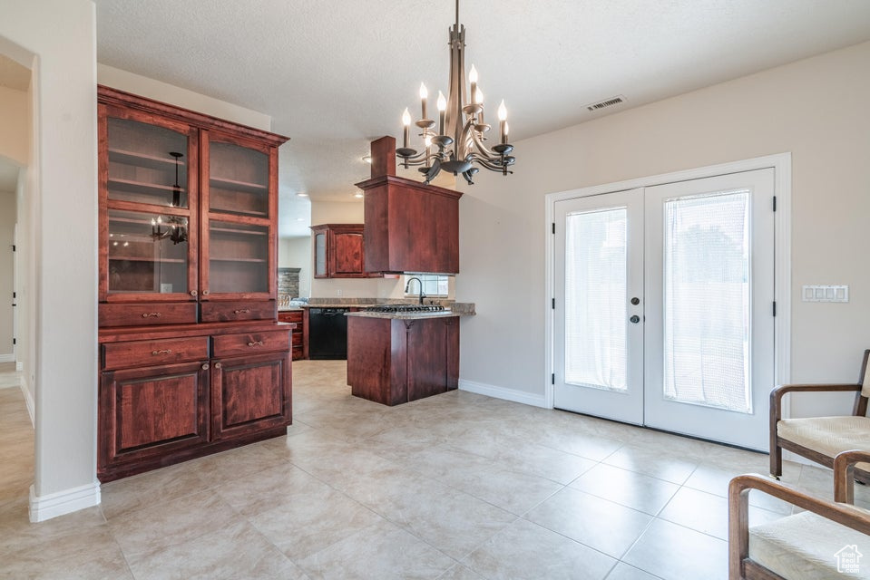 Kitchen with light tile patterned floors, french doors, a notable chandelier, kitchen peninsula, and pendant lighting