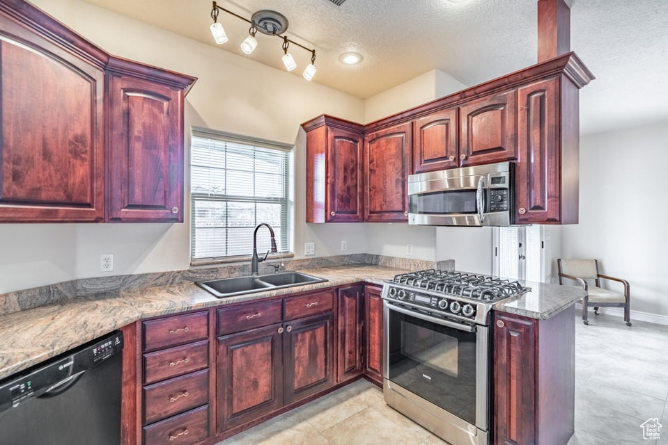 Kitchen featuring appliances with stainless steel finishes, sink, track lighting, light tile patterned flooring, and a textured ceiling