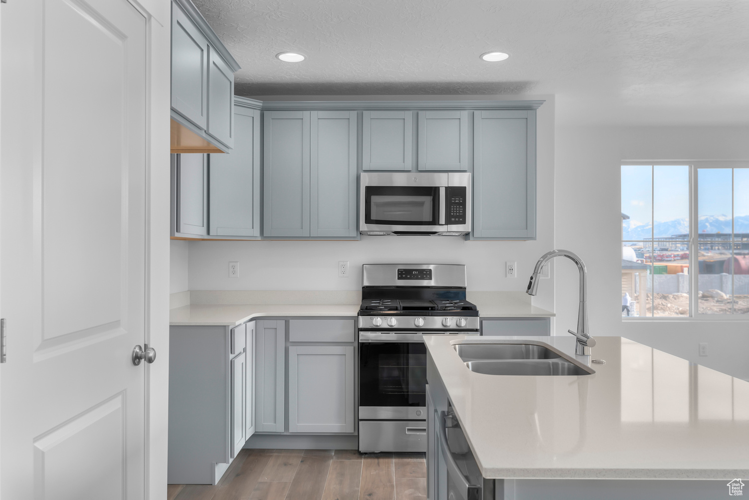 Kitchen featuring light wood-type flooring, gray cabinetry, a textured ceiling, stainless steel appliances, and sink