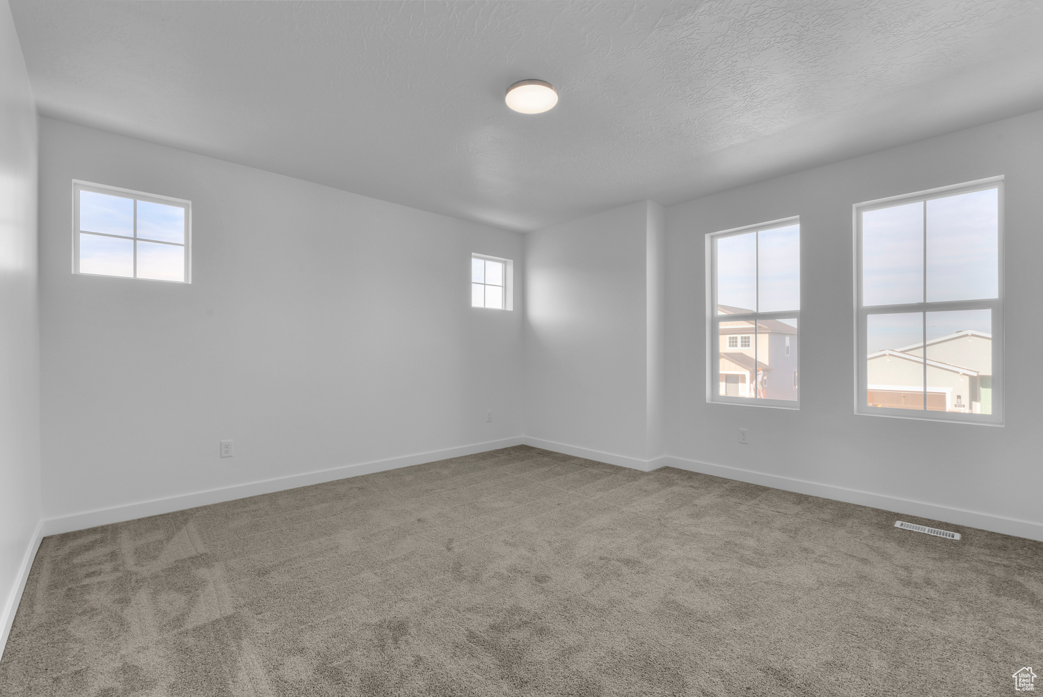 Unfurnished room with a textured ceiling, carpet floors, and a healthy amount of sunlight